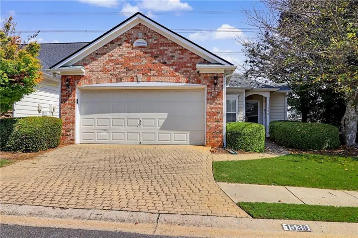 Brick and siding exterior with an attached garage, paver driveway, and manicured landscaping