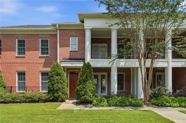 Brick exterior with white columns, a wood-finish front door, and manicured landscaping