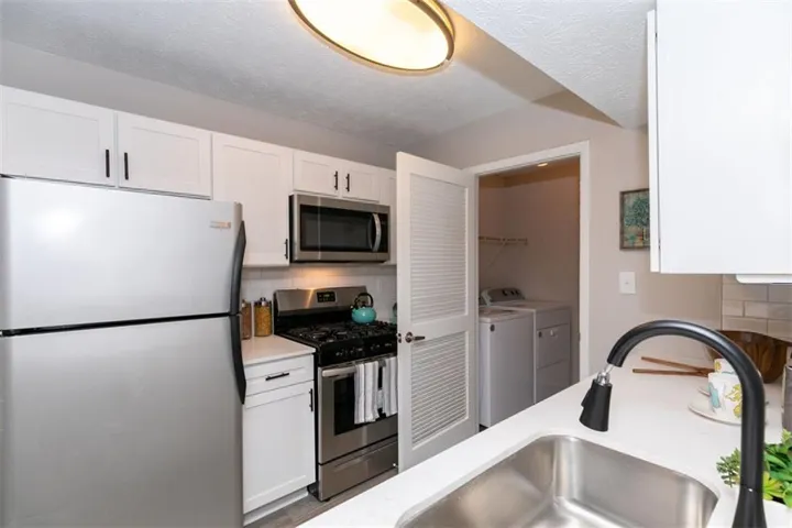 Stainless steel appliances, white cabinetry, undermount sink, white countertops, and a full-size washer and dryer