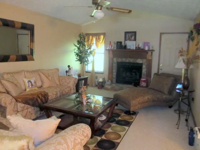 Vaulted ceiling with a ceiling fan, stone-faced fireplace with a wood mantle, and light-toned wall finishes