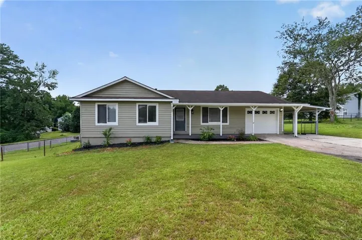 Ranch-style residence featuring light-colored siding, an attached garage, a car port, and a dark-colored shingle roof
