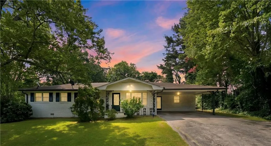 White brick ranch-style residence featuring a covered carport, mature trees, manicured lawn, and dark shutters