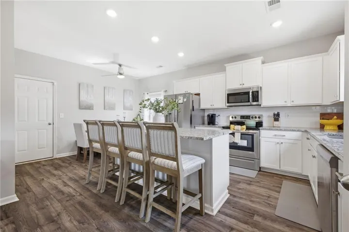 Kitchen featuring an island with stone-finish countertop, white cabinetry, stainless steel appliances, wood-finish flooring, and recessed lighting