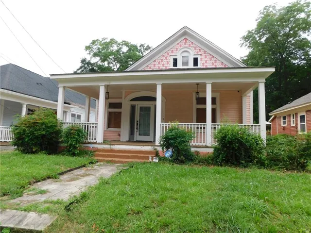 Classic architectural style featuring a covered front porch with white railings and columns, a decorative pediment with patterned shingles, and a central entry door with an arched transom