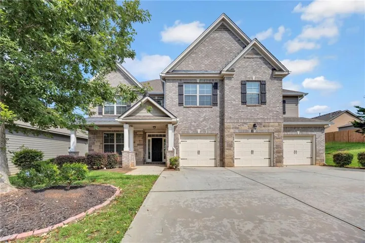 Two-story residence featuring a brick and stone facade, three garage bays, a covered entry, and mature landscaping