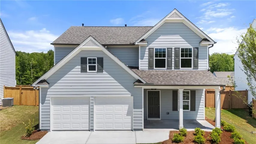 Two-story exterior with light blue siding, dual garage doors, covered front entry, dark shutters, and a sloped roofline