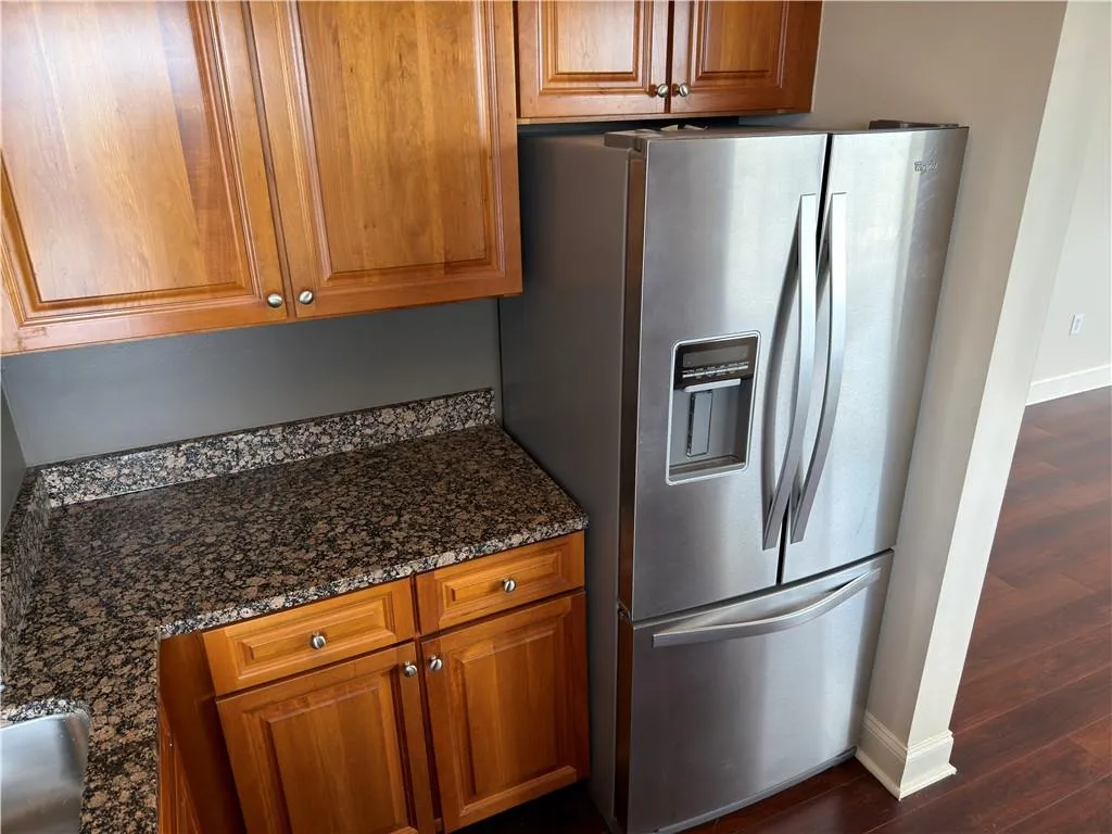 Kitchen with wood finish cabinetry, stainless steel refrigerator with ice dispenser, dark stone counters, and dark wood-style floors