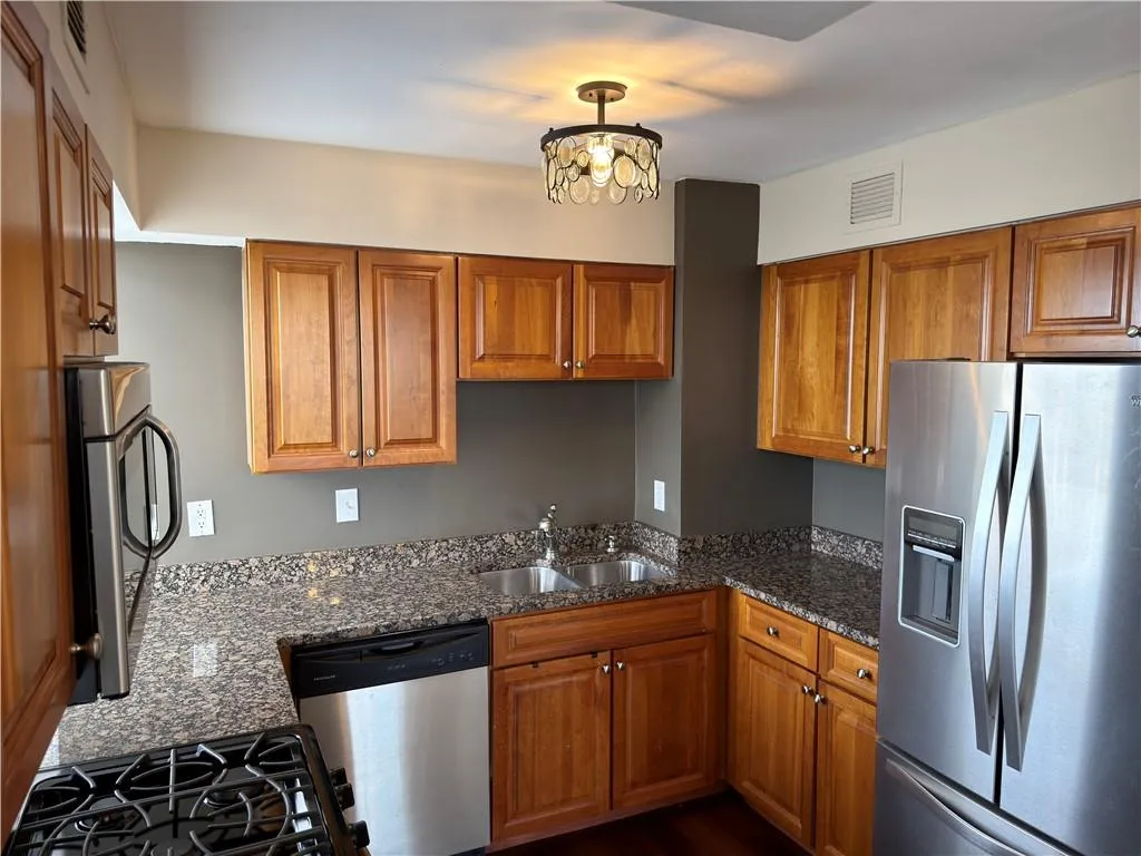 Kitchen featuring stainless steel appliances, wood finish cabinets, dark stone countertops, and hanging light fixtures
