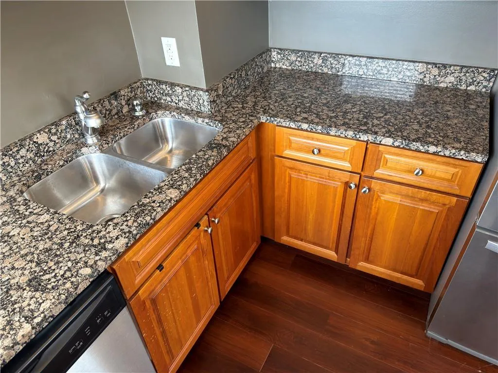 Kitchen with wood finish cabinets, stainless steel dishwasher, dark stone countertops, and dark wood-type flooring