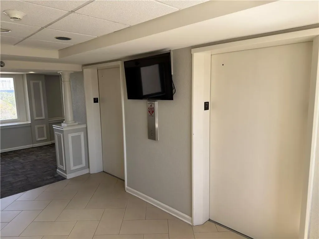 Corridor with elevator, a paneled ceiling, light tile patterned flooring, and decorative columns