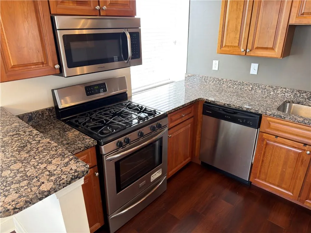 Kitchen with stainless steel appliances, dark stone countertops, and wood finish cabinetry