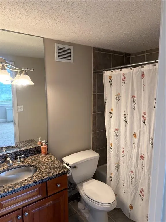 Bathroom featuring a textured ceiling, vanity, shower / tub combo, and tile patterned floors
