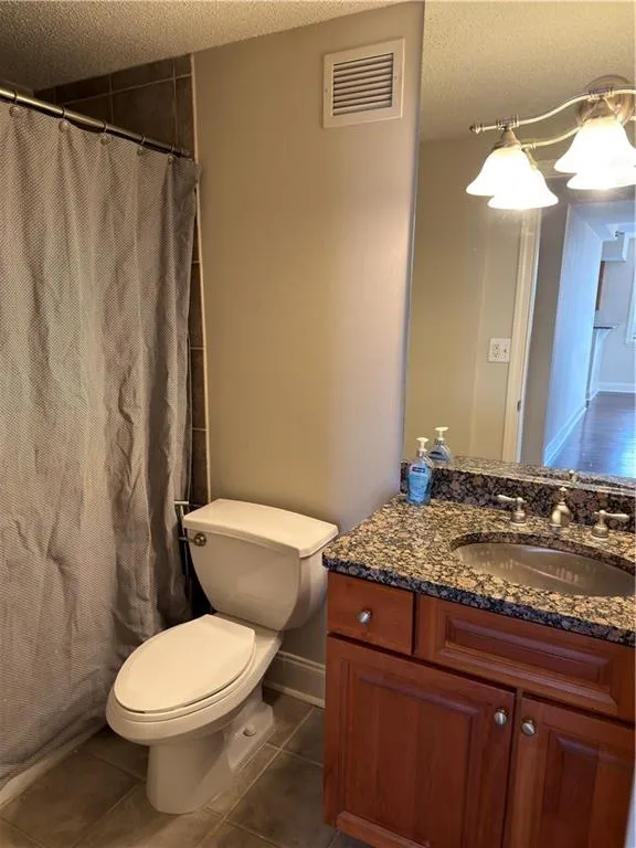 Full bathroom featuring a textured ceiling, vanity, a shower with shower curtain, and dark tile patterned flooring