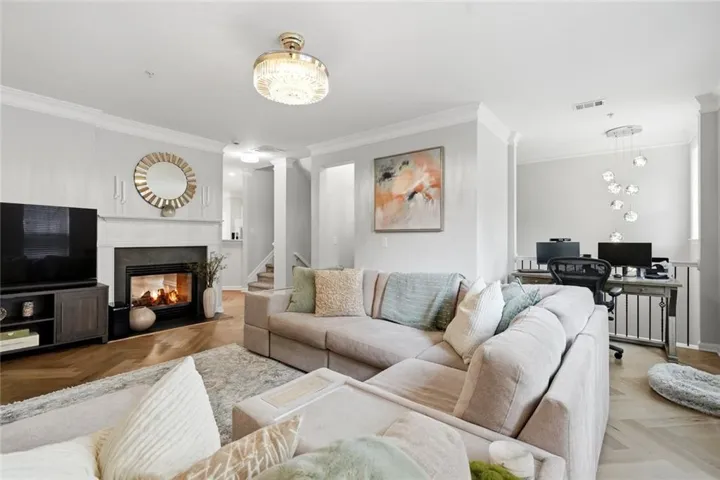 Living area featuring a fireplace with a white mantel, chevron wood-finish flooring, and crown molding