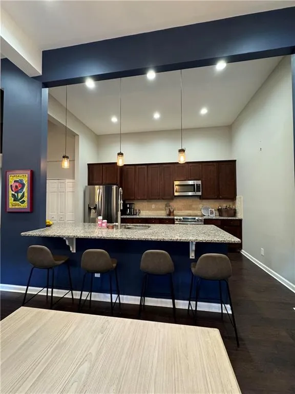 Kitchen featuring appliances with stainless steel finishes, decorative light fixtures, light stone countertops, and dark wood-type flooring
