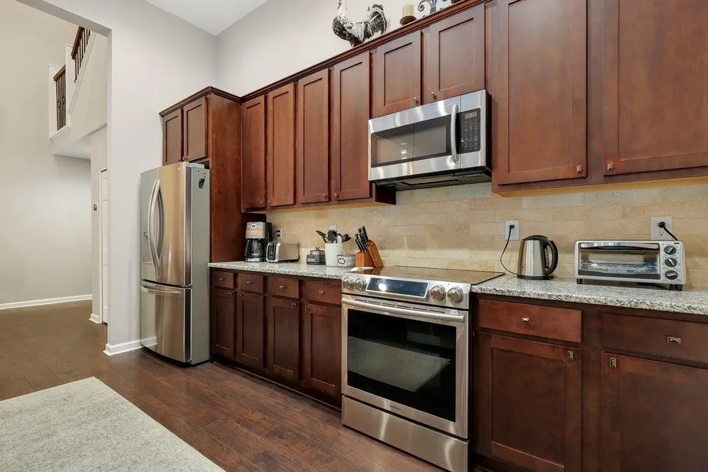 Kitchen with decorative backsplash, appliances with stainless steel finishes, dark hardwood / wood-style floors, and light stone counters