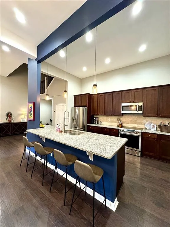 Kitchen featuring a breakfast bar area, appliances with stainless steel finishes, dark hardwood / wood-style floors, and light stone countertops