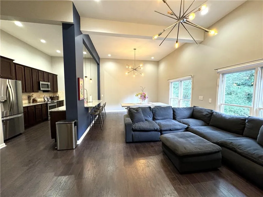 Living room featuring dark wood-type flooring, a notable chandelier, and high vaulted ceiling