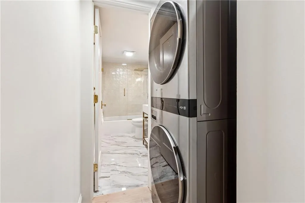 Laundry area featuring stacked washing machine and dryer and light marble finish floors