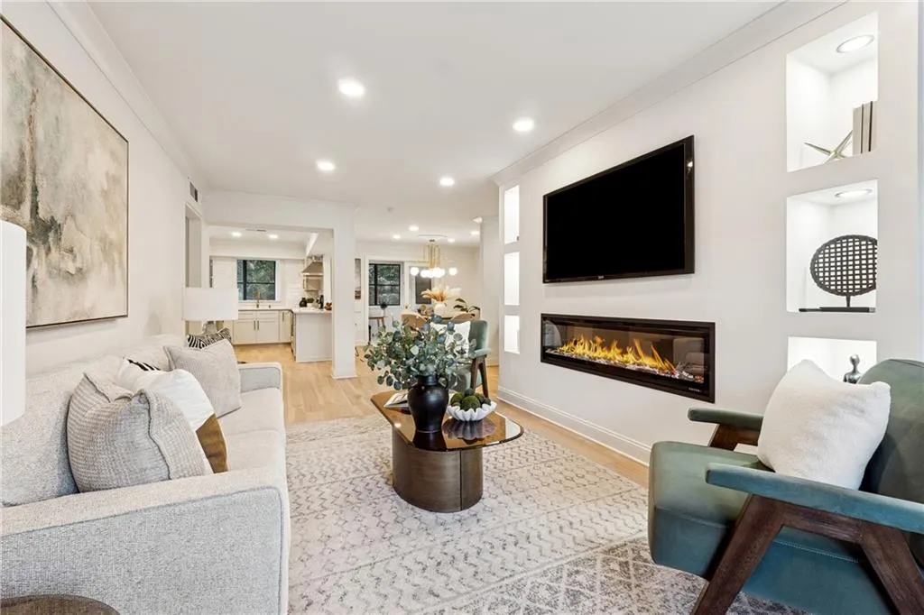 Living room with light wood-style floors, a glass covered fireplace, crown molding, recessed lighting, and a chandelier