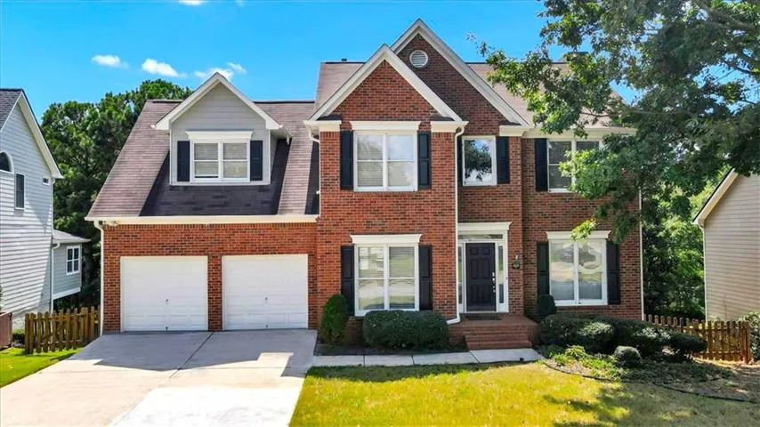 Brick exterior with white trim, two-car garage, front porch, and mature landscaping