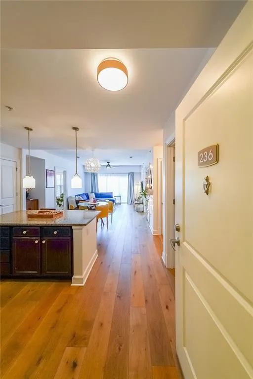 Kitchen featuring light stone counters, dark brown cabinets, light wood-style flooring, hanging light fixtures, and open floor plan