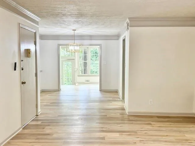 Hall featuring a chandelier, a textured ceiling, ornamental molding, and light wood-style flooring