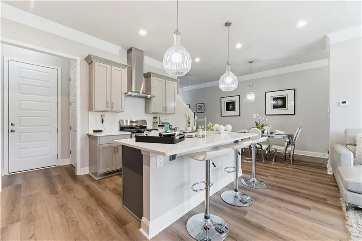 Kitchen featuring gray cabinets, a kitchen bar, hanging light fixtures, light wood-type flooring, and ornamental molding