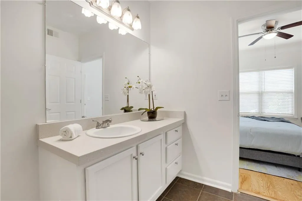 Ensuite bathroom featuring vanity, dark tile patterned flooring, and a ceiling fan