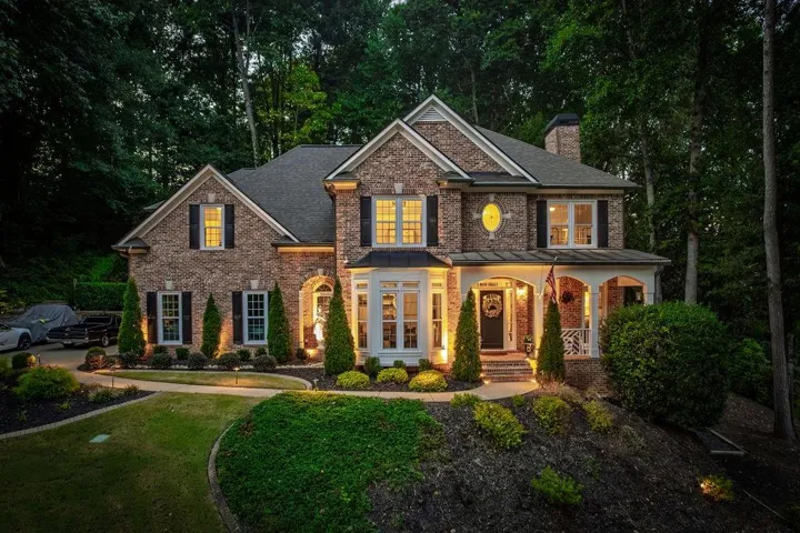 Elegant brick Colonial estate featuring a welcoming front facade with arched entryway, multi-pane illuminated windows, and professional landscape lighting