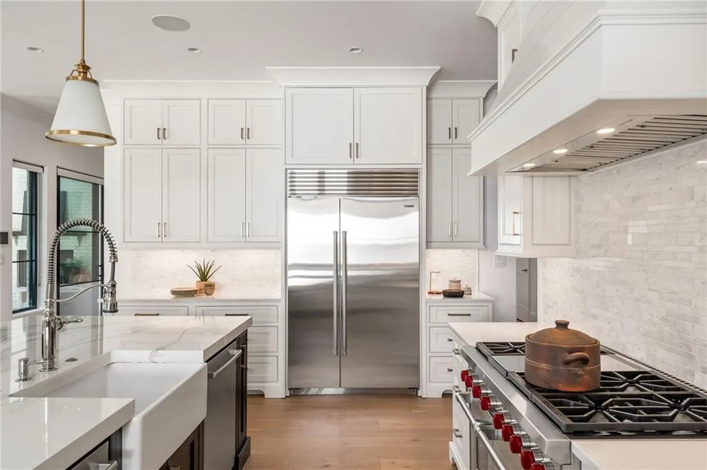Kitchen with a sink, high quality appliances, white cabinetry, custom exhaust hood, and decorative light fixtures