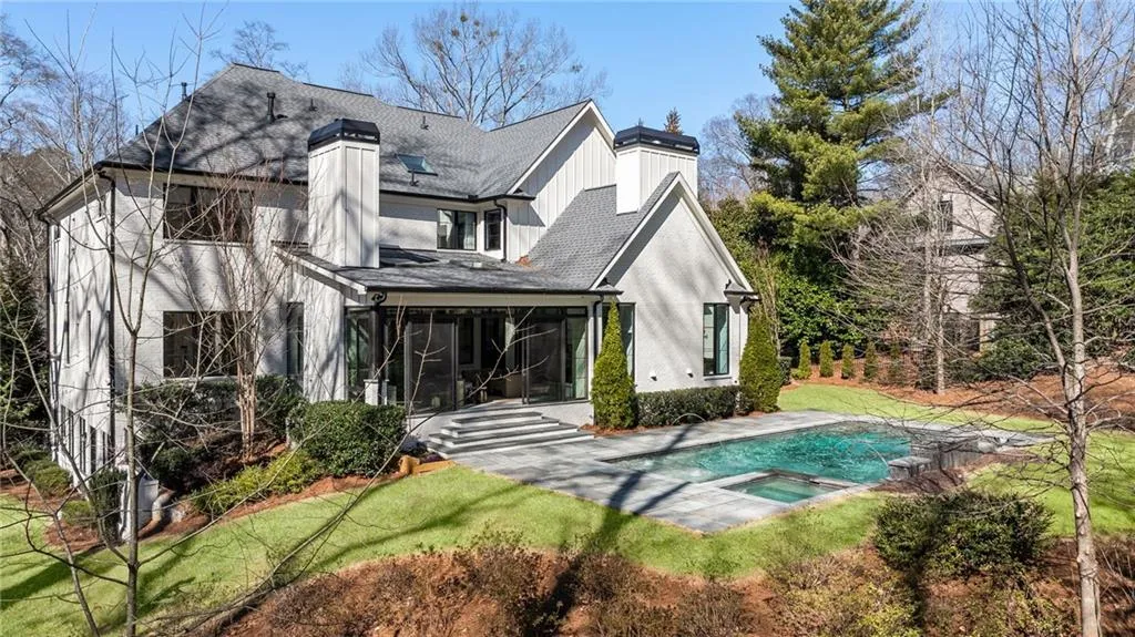 Rear view of house with a pool with connected hot tub, a sunroom, a lawn, and a chimney