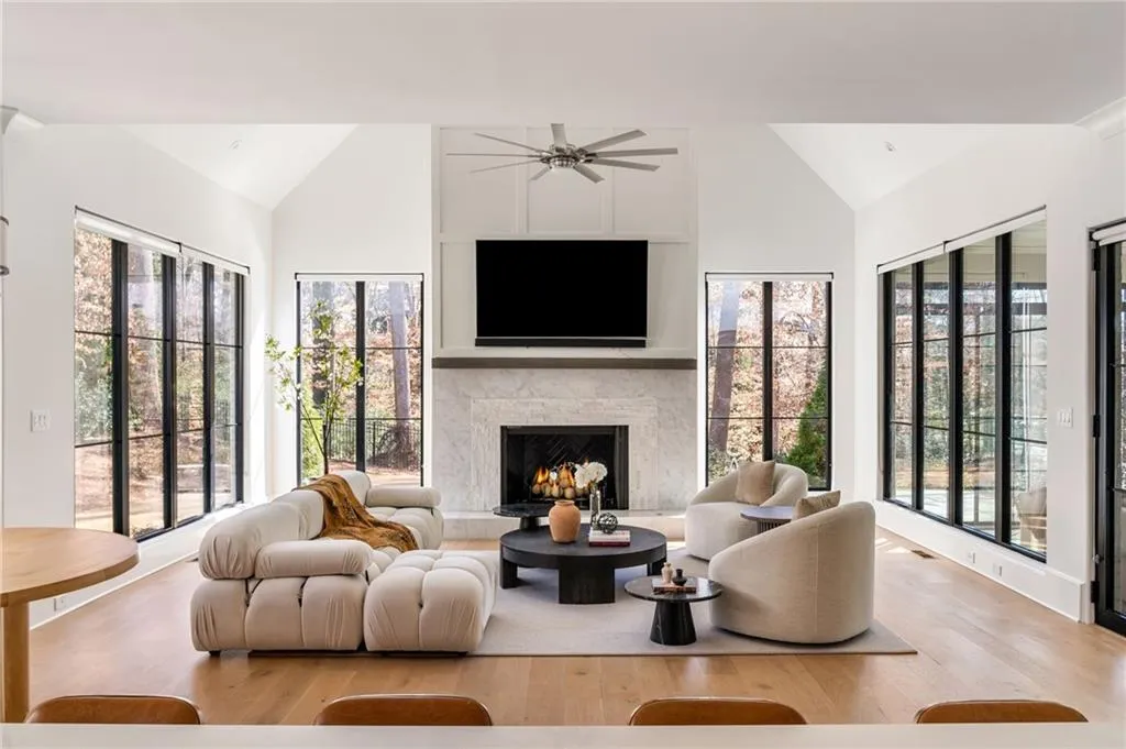 Living room with a lit fireplace, high vaulted ceiling, and wood finished floors