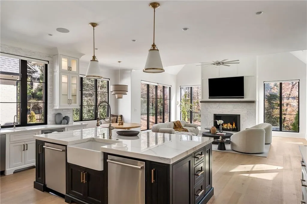 Kitchen with a warm lit fireplace, a sink, light wood-style floors, white cabinets, and a center island with sink