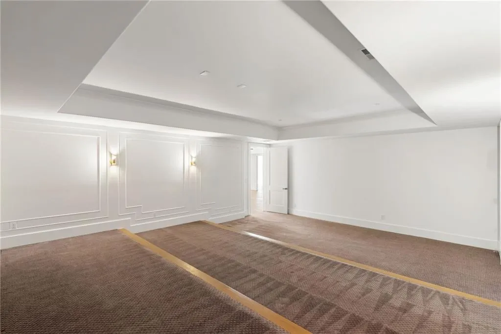 Empty room with carpet floors, a raised ceiling, a decorative wall, and baseboards