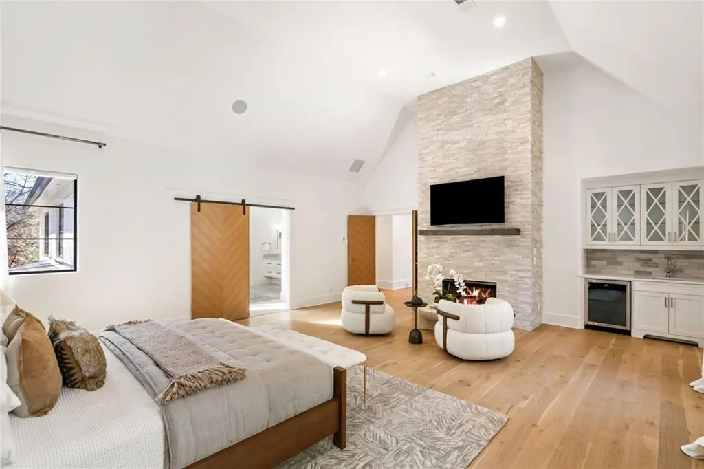 Bedroom with a fireplace, a barn door, high vaulted ceiling, light wood-type flooring, and beverage cooler