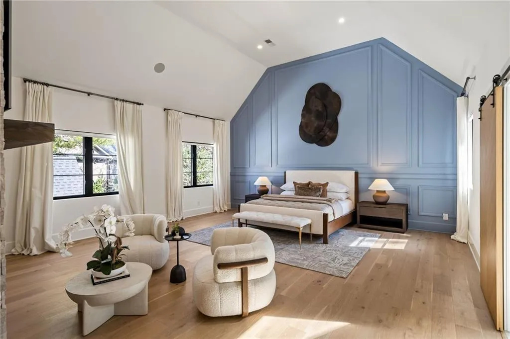 Bedroom with light wood-style floors, a barn door, vaulted ceiling, and a decorative wall