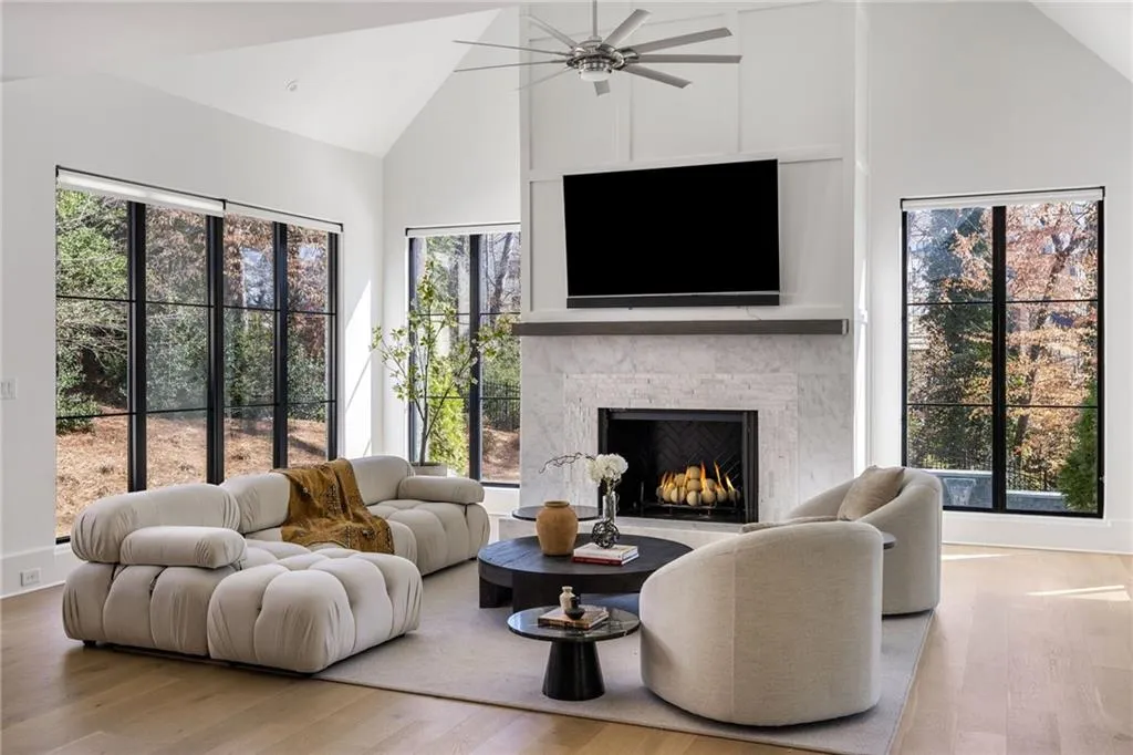 Living room featuring high vaulted ceiling, a warm lit fireplace, and wood finished floors