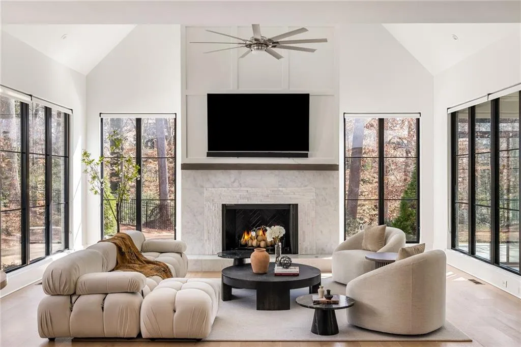 Living area with high vaulted ceiling, a warm lit fireplace, visible vents, and wood finished floors