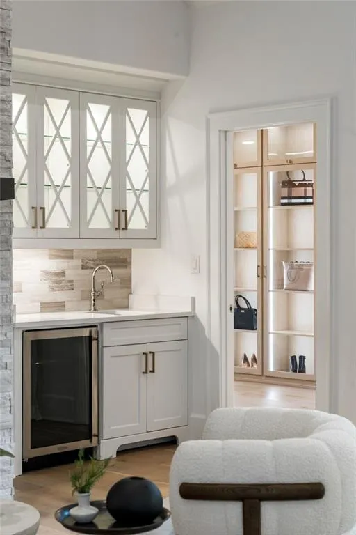 Bar with beverage cooler, a sink, wood finished floors, wet bar, and tasteful backsplash