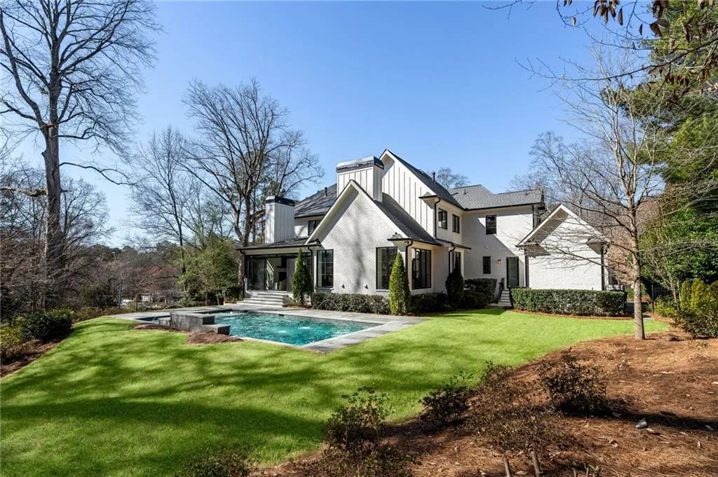 Back of property featuring board and batten siding, an outdoor pool, a lawn, and a chimney