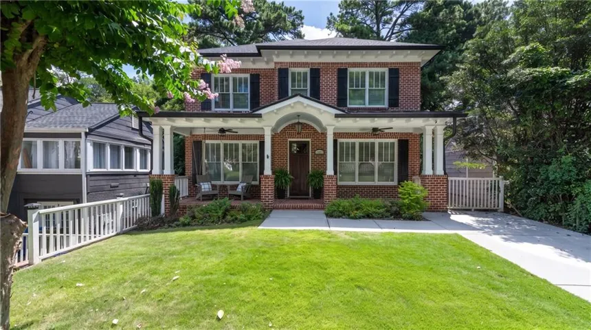 Brick facade residence featuring a covered front porch with white columns, a dark wood entry door, and a manicured lawn