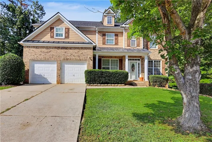 Brick and siding exterior with a covered porch, two-car garage, and mature landscaping
