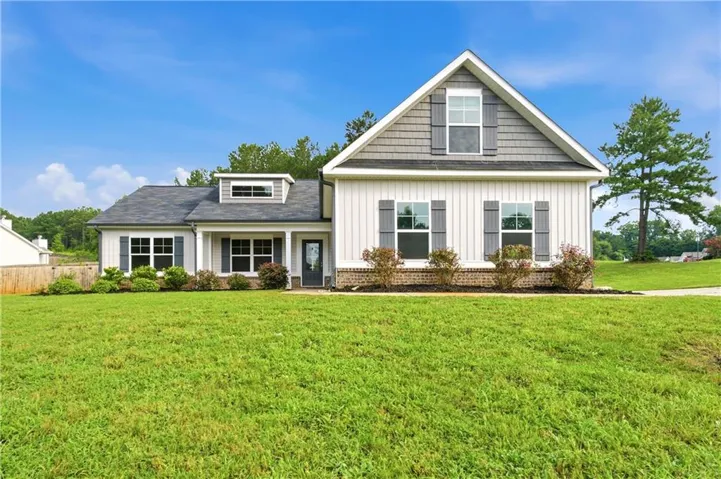 Contemporary farmhouse exterior featuring white board-and-batten siding, gray shingle accents, dark gray shutters, a brick foundation, and a wide front lawn