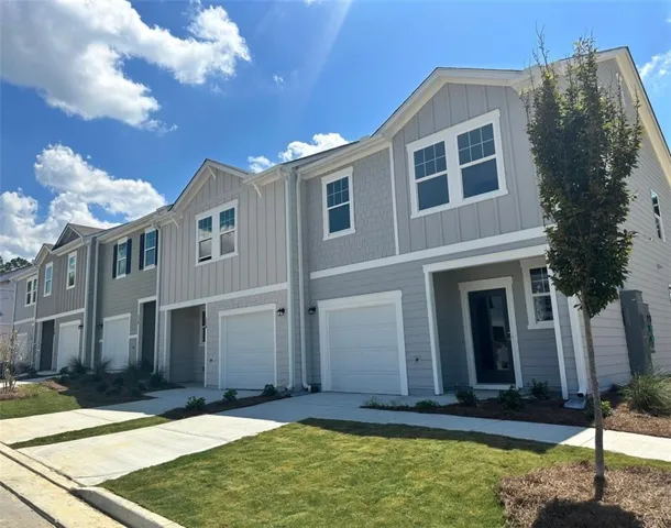 Contemporary townhome exterior featuring light gray siding with vertical and shingle accents, white trim, attached garage, and a concrete driveway