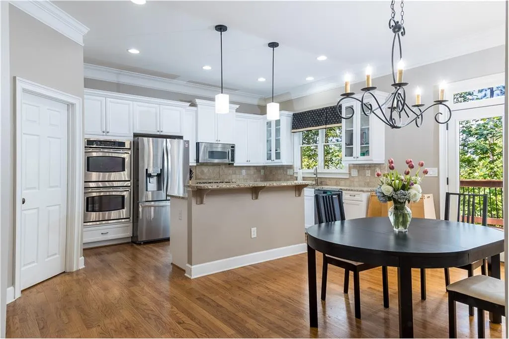 Kitchen with glass insert cabinets, a kitchen bar, pendant lighting, light stone countertops, and white cabinetry