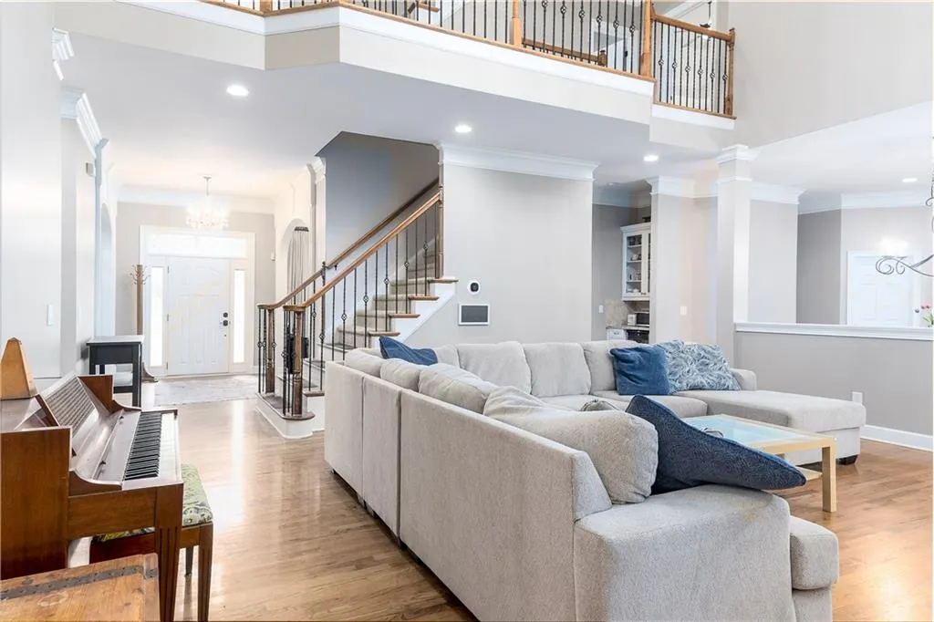 Living area featuring a chandelier, a towering ceiling, ornamental molding, light wood-type flooring, and recessed lighting