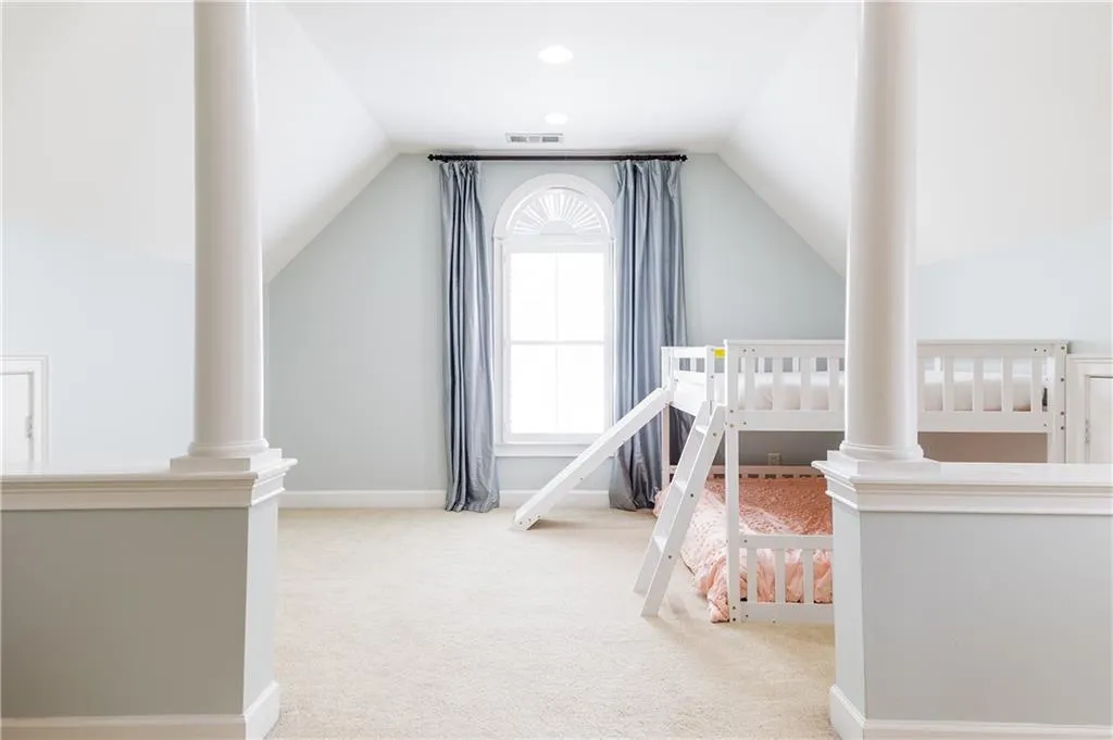 Carpeted bedroom with ornate columns and vaulted ceiling