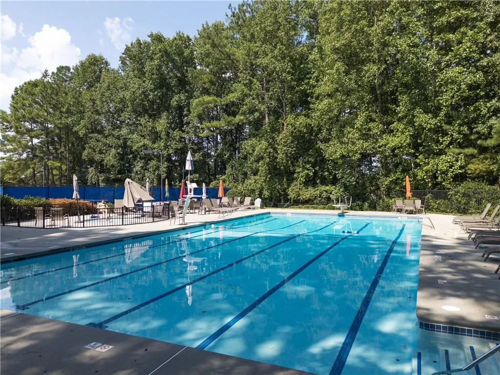 Community pool with a patio area and view of wooded area