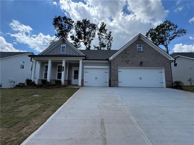 Exterior featuring brick and siding finishes, a covered front porch with columns, a two-car garage with white doors, and a concrete driveway